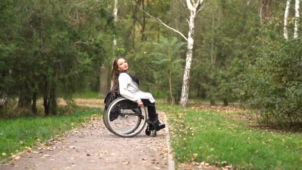 Attraktives Mädchen im Rollstuhl, das im Herbstpark spazieren geht. Behinderte Freizeit — Stockvideo