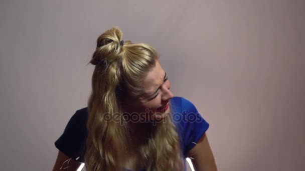Сексуальная девушка-блондинка в синем платье смеется над своей невероятной шуткой в студии со светлым фоном. Мотивационное видео — стоковое видео