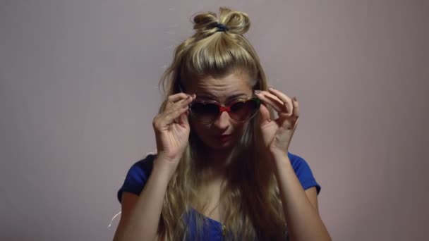 Belle fille blonde sexy en robe bleue posant en forme d'amour Lunettes de soleil Studio avec fond clair . — Video