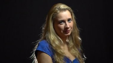 Mavi elbiseli güzel seksi sarışın kız flört ve siyah arka plan ile Studio için Winking olduğunu.