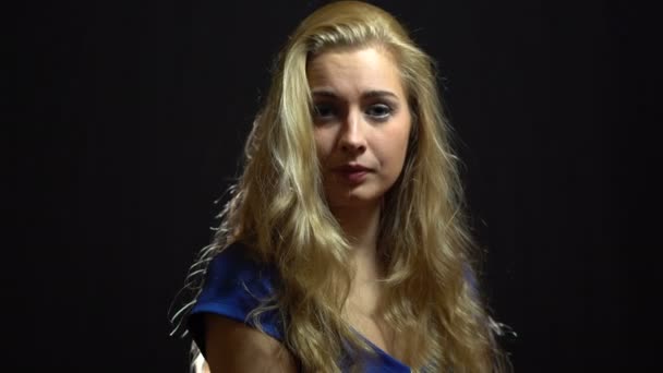 Piękna Sexy blondynka dziewczyna w niebieskiej sukience jest Flirting i patrząc wokół, w Studio z czarnym tłem. — Wideo stockowe