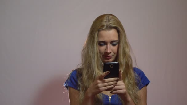 Mooie Sexy blond meisje in blauwe jurk chatten met telefoon in Studio — Stockvideo
