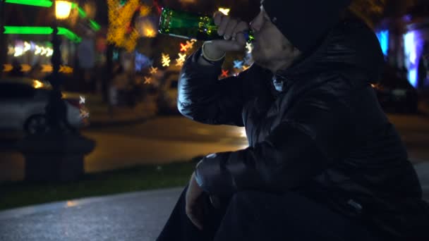 Genç adam bakarak otururken, gece sokak ve içme bira şişe formu. — Stok video