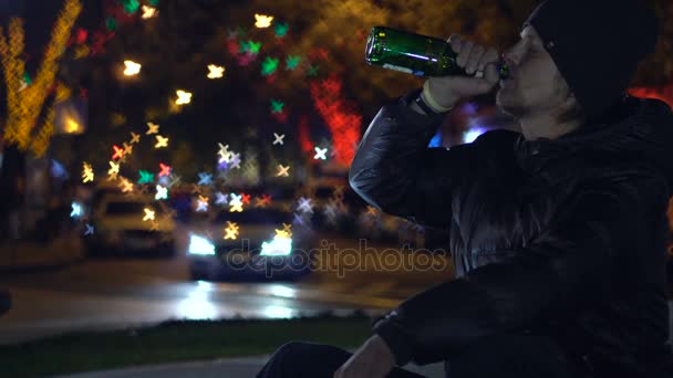 Jonge man zitten, kijken naar de de nacht Street en drinken bier vormen de fles — Stockvideo