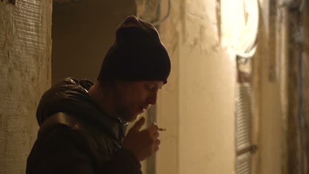 Молодой парень курит табак ручной прокатки CIgarette в доме ворота, холодная погода ночь города — стоковое видео