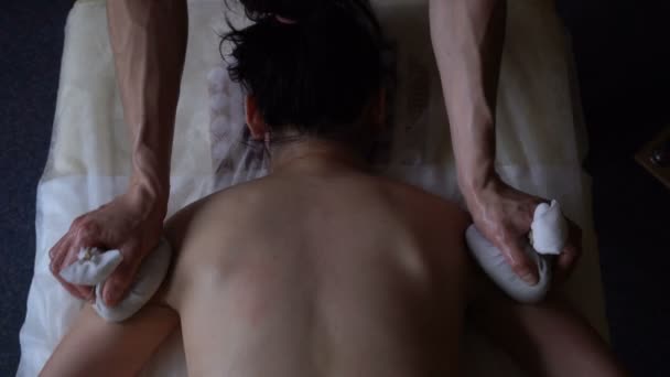 Professionele Masseur kneedt de schouders van jonge vrouw met Rag zakken tijdens de zitting van de Massage. Ayurvedic Abyanga massage. — Stockvideo