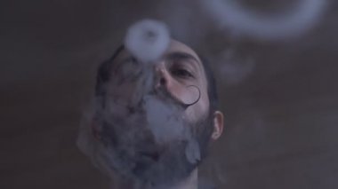Sakal ve Mustages Vaping elektronik sigara olan genç adam. Vaper Hipster duman Buharlaştırıcı ve Exhals duman halkaları.