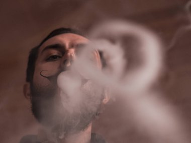 Sakal ve Mustages Vaping elektronik sigara olan adam. Vaper Hipster duman Buharlaştırıcı ve Exhals duman halkaları.