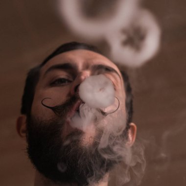 Sakal ve Mustages Vaping elektronik sigara olan adam. Vaper Hipster duman Buharlaştırıcı ve Exhals duman halkaları.