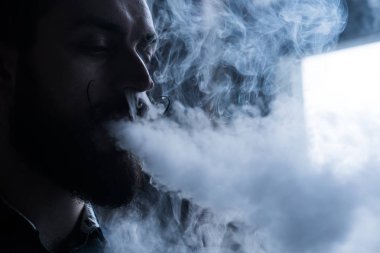 Sakal ve Mustages Vaping elektronik sigara olan adam. Vaper Hipster duman Buharlaştırıcı ve Exhals duman akış.