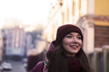 Çok gülümseyen esmer kız mor kış ceket, şapka ve atkı, Avrupa Street tarafından kış yürüyüş giyiyor