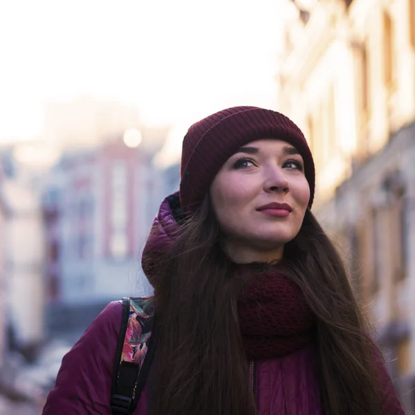 Güzel esmer kız mor kış ceket, şapka ve atkı, Avrupa Street tarafından kış yürüyüş giyiyor — Stok fotoğraf