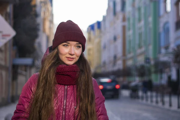 Güzel esmer kız mor kış ceket, şapka ve atkı, Avrupa Street tarafından kış yürüyüş giyiyor — Stok fotoğraf