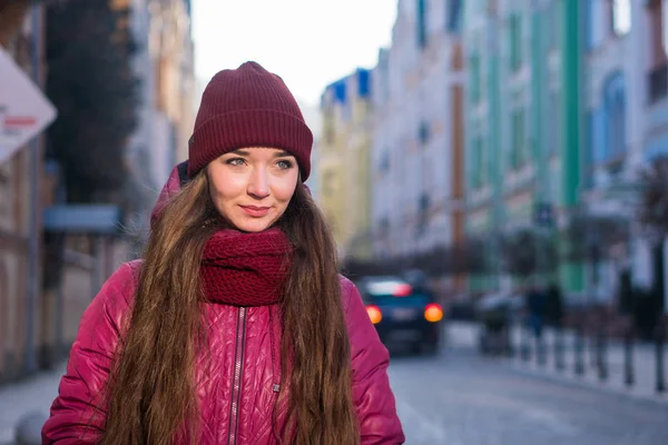 Çok gülümseyen esmer kız mor kış ceket, şapka ve atkı, Avrupa Street tarafından kış yürüyüş giyiyor — Stok fotoğraf