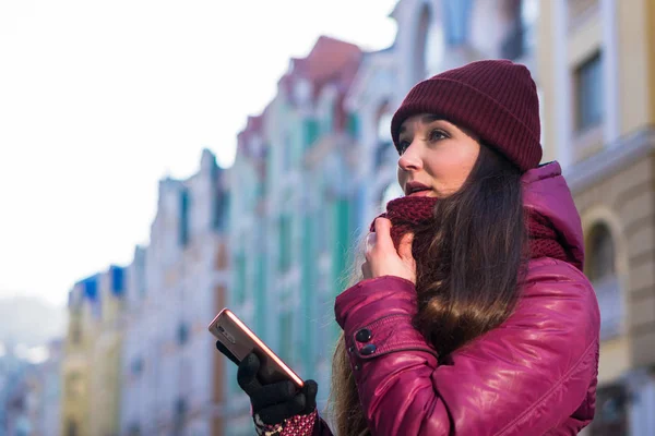 Güzel esmer kız giyiyor mor kış ceket, şapka ve atkı, Avrupa Street tarafından kış yürüyüş, fotoğraf Her Smartphone ve yapım Selfie yapmak — Stok fotoğraf