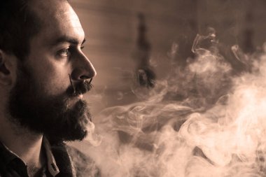 Sakal ve Mustages Vaping elektronik sigara olan adam. Vaper Hipster duman Buharlaştırıcı ve Exhals duman halkaları.