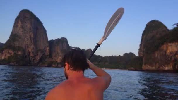 Powrót widzenia silnego człowieka na kajak w wodzie na otwarte morze. Zachód słońca nad urwisk skalnych. Railay Beach, Krabi, Tajlandia. — Wideo stockowe