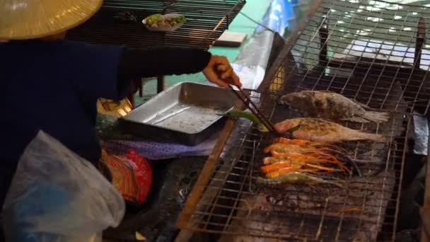 Una mujer tailandesa en paño tradicional cocinando camarones grandes en un fuego de barbacoa en el barco en Floating Market, Bangkok . — Vídeo de stock