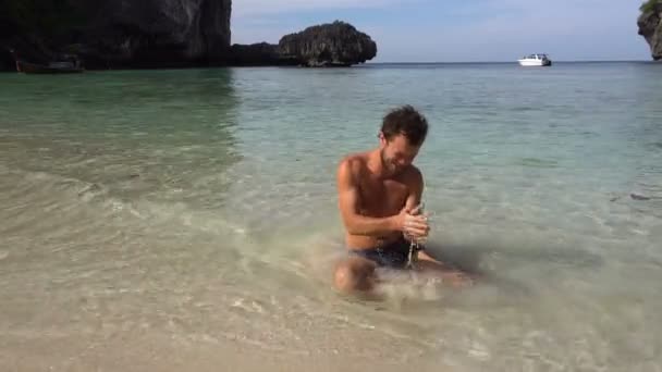 Man ontspannen op het strand van wit zand, spelen met zand, gewassen met warme azuurblauwe oceaanwater. — Stockvideo