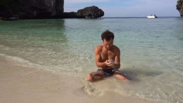 Hombre relajante en la arena blanca de la playa, jugar con la arena, lavado con agua caliente del océano azul . — Vídeos de Stock