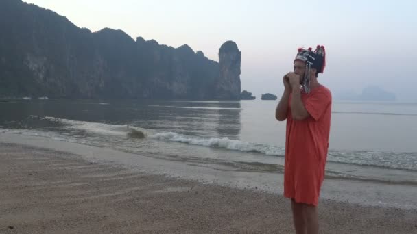 Freaky kaukázusi Férfi hagyományos Thai női kalap játszik a hárfa a reggel Twilight, a partvidék, gyönyörű trópusi sziklás Cliff lagúna-Krabi, Thaiföld. — Stock videók