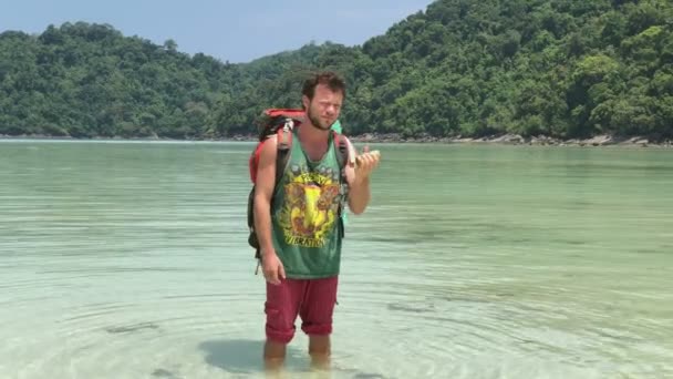 Uomo escursionista felice con zaino turistico che gioca sul suo shaker in acqua calda della laguna tropicale azzurra — Video Stock