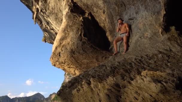 Tapferer Abenteurer spielt barfuß auf dem Hang der scharfen Insel Kalksteinhöhle in der Krabi, Thailand mit Felsen von Railey Beach im Hintergrund. — Stockvideo