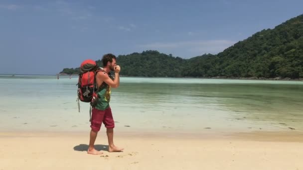 Uomo escursionista felice con zaino turistico Giocare sulla sua arpa mentre si cammina lungo la costa di acqua calda Laguna tropicale azzurra — Video Stock