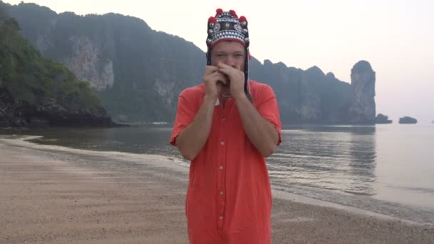 Freaky Caucasian Man in Traditional Thai Womens Hat Playing on his Harp at the Morning Twilight on the Coastline of Beautiful Tropical Rocky Cliff Lagoon in Krabi, Tailandia . — Vídeos de Stock