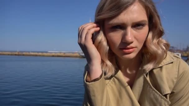 Porträt der attraktiven jungen blonden Frau im Schützengraben mit Vintage-Koffer sitzt auf der Seebrücke — Stockvideo