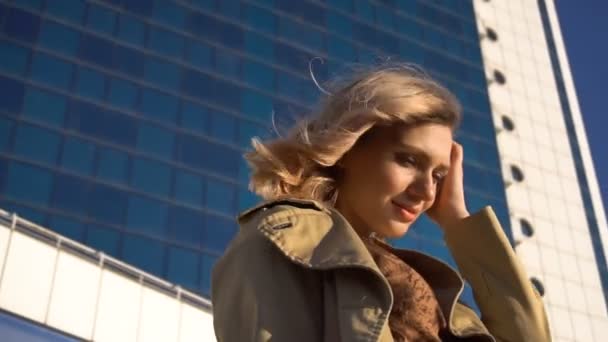 Aantrekkelijke jonge Blonde vrouw in de loopgraaf en hoge hak schoenen met Vintage koffer op het Marine Station, met hoge blauw glas Hotel op achtergrond. — Stockvideo