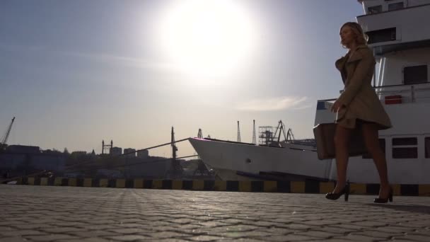 Atractiva joven mujer rubia feliz en trinchera con maleta vintage caminando y saltando en el muelle Jacht — Vídeos de Stock