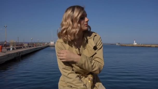 Approche de attrayant jeune femme blonde dans la tranchée avec valise Vintage est assis sur la jetée de bateau — Video