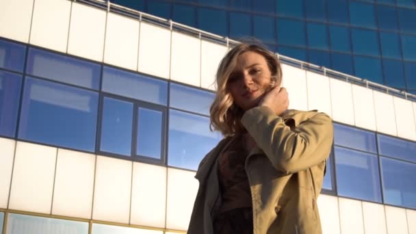 Attractive Young Blonde Woman in Trench and High Heel Shoes with Vintage Suitcase Spinning on the Marine Station, with High Blue Glass Hotel on Background. Low Angle — Stock Video