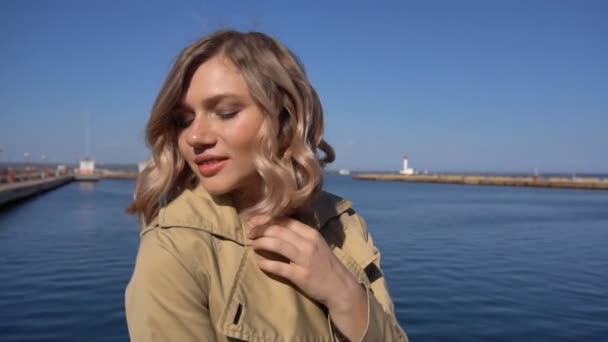 Cabelo Fluttering de mulher loira jovem atraente em trincheira com mala vintage — Vídeo de Stock