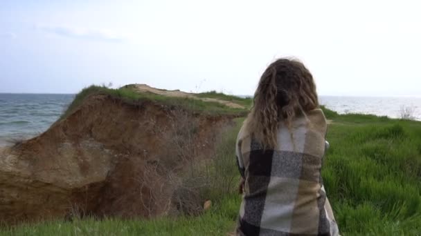 Glad ung kvinna i röd klänning insvept i en matta har kul på havet kusten klippan — Stockvideo