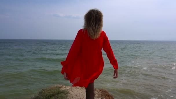 Šťastný, mladá žena v červené šaty, krouží a bavit se na útesu pobřeží moře — Stock video