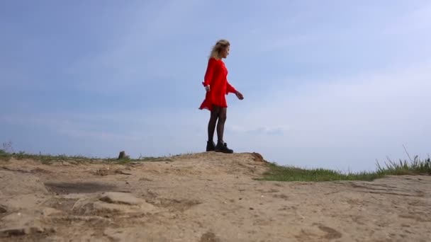 Blíží se šťastná dívka v červených šatech bavit na pobřeží moře útesu — Stock video