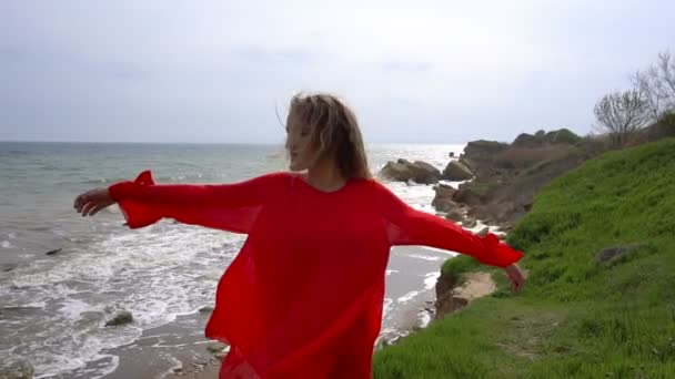 Mujer joven feliz en vestido rojo dando vueltas y divertirse en el acantilado de la costa del mar — Vídeo de stock