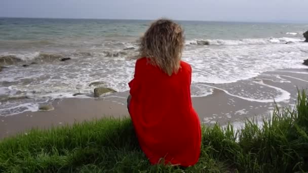 红色礼服的愉快的年轻妇女有乐趣在海海岸和坐在悬崖上 — 图库视频影像