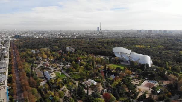 Flying over Louis Vuitton Foundation museum modern building in Paris, France (en inglés). Torre Eiffel en el fondo, bosque de Boulogne alrededor . — Vídeos de Stock