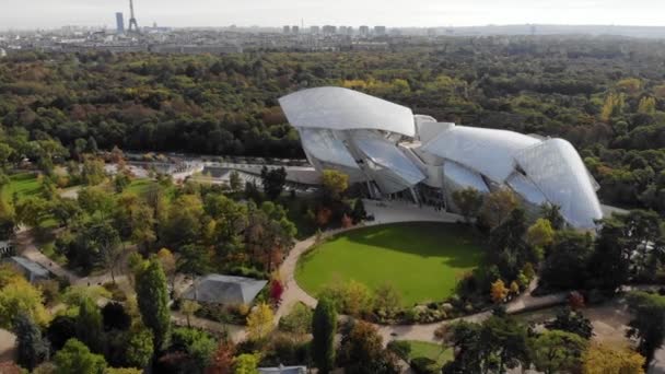 Flying over Louis Vuitton Foundation museum modern building in Paris, France (en inglés). Torre Eiffel en el fondo, bosque de Boulogne alrededor . — Vídeo de stock