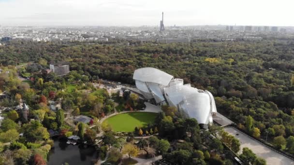 Flying over Louis Vuitton Foundation museum modern building in Paris, France (en inglés). Torre Eiffel en el fondo, bosque de Boulogne alrededor . — Vídeos de Stock