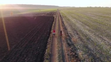 Kırsal bölgedeki tarlaları geçtikten sonra bisikletli çocukların üzerinde uçan hava aracı. Altın saat.
