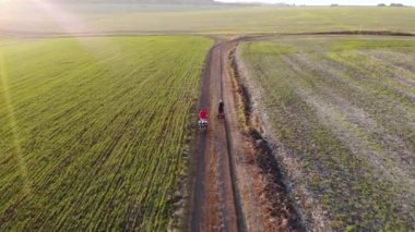Kırsal bölgedeki tarlaları geçtikten sonra bisikletli çocukların üzerinde uçan hava aracı. Altın saat.