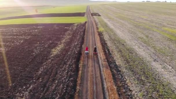 Letecký létání nad chlapci na kole na vyjeté silnici kolem polí na venkově. Zlatá hodina. — Stock video