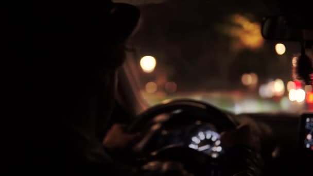 Homem de chapéu elegante dirigindo um carro em Paris à noite, com luzes de rua noturnas brurred — Vídeo de Stock