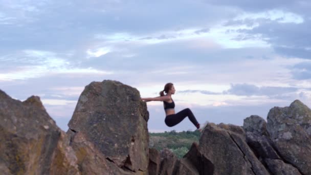 Mulher desportiva praticando ioga e ginástica exercícios em penhasco de montanha com bela paisagem ob fundo. Estilo de vida saudável. extremo ativo . — Vídeo de Stock