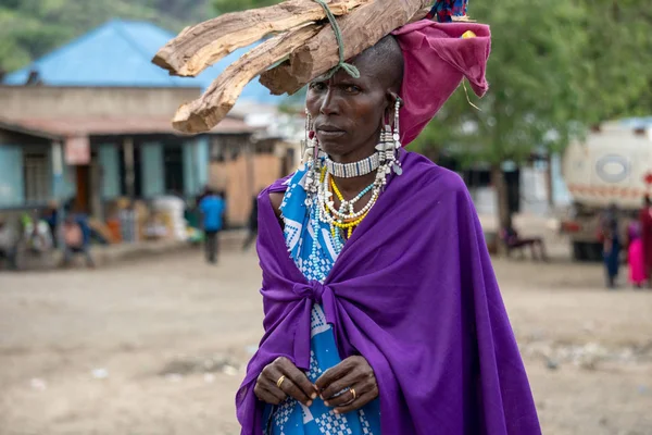 TANZÂNIA, MASAI VILLAGE - JANEIRO 2020: mulher com troncos na cabeça na aldeia nativa de Masai Engare Sero, na costa do Lago Natron, em Maas=, distrito de Arusha — Fotografia de Stock