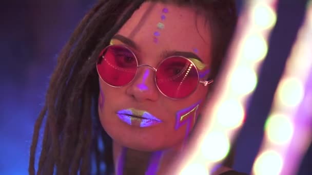 Portret van een meisje met dreadlocks in Neon UF Light. Model Meisje dansen met een LED uitgeleend is Red Sunglasses, Art Design of Female Disco Dancer Model in UV, Kleurrijk Abstract Make-up. — Stockvideo